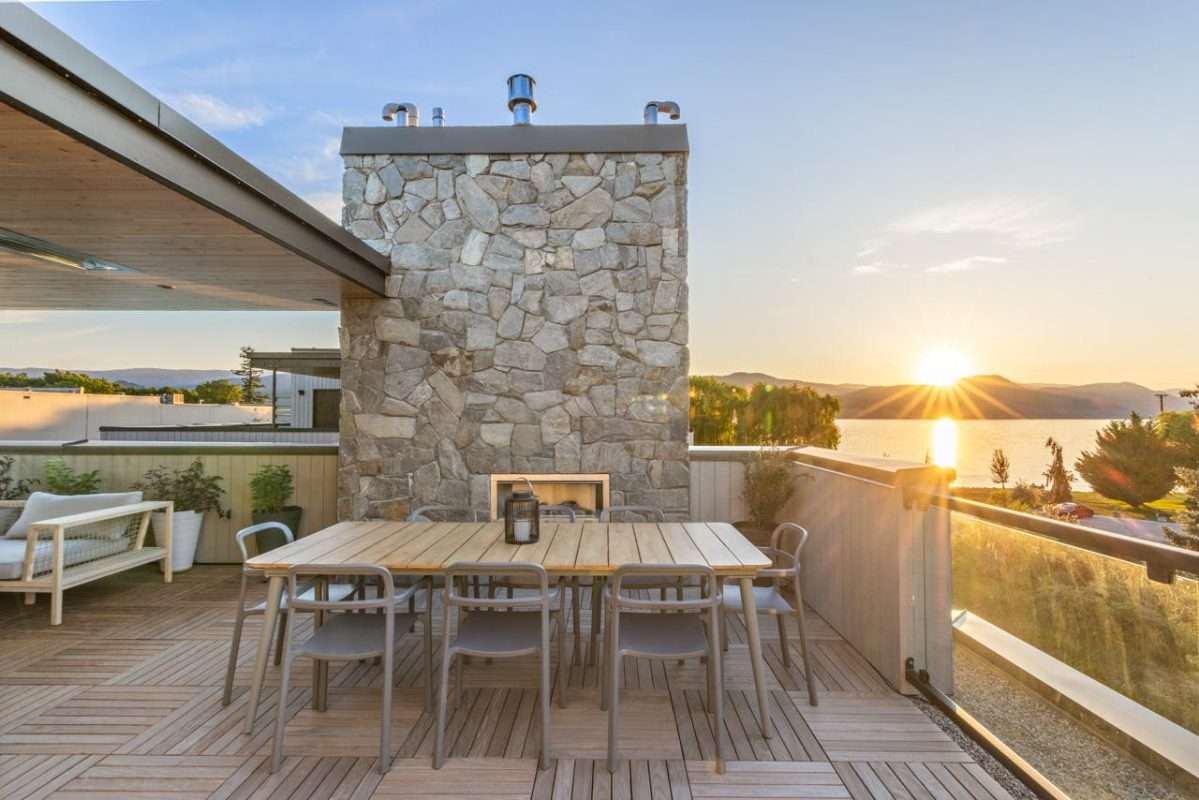 Rooftop patio with ledgestone fireplace feature wall, wood deck tiles and lake sunset view